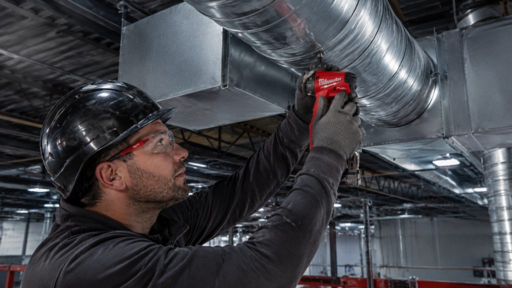 Milwaukee M12 FUEL FDDX befestigt Lüftungsrohre in einer Industriehalle