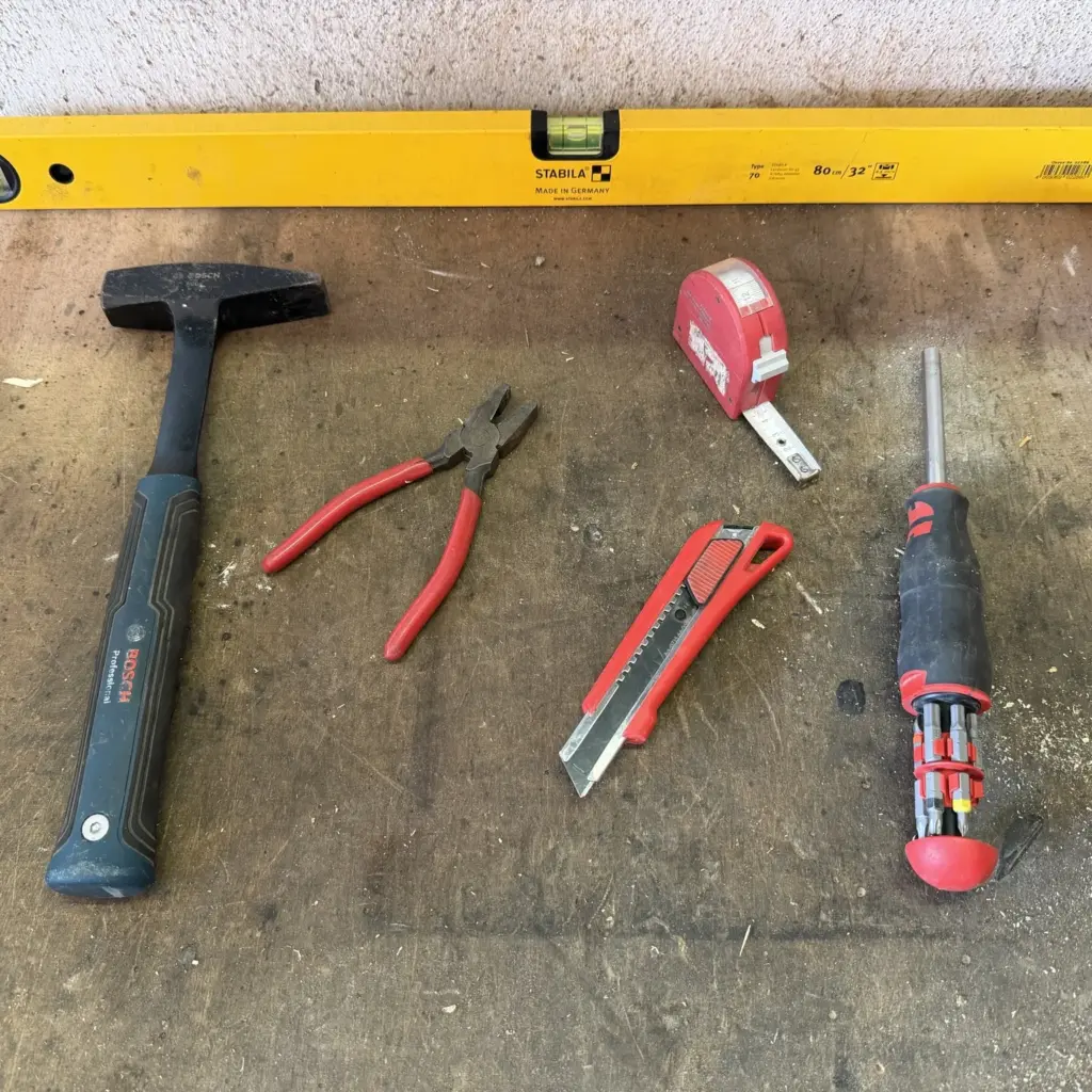 Hammer, Kombizange, Maßband, Cuttermesser, Bit-Schraubendreher und Stabila-Wasserwaage auf einer gebrauchten Werkbank