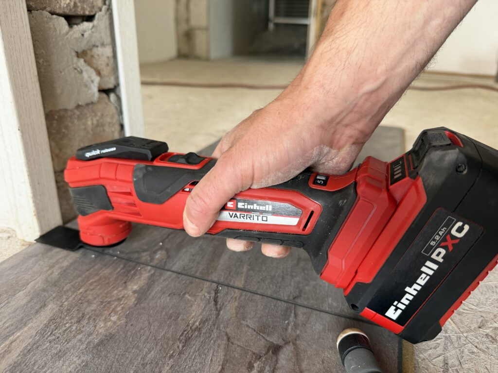 Einhell Varrito Multitool unterschneidet eine Türleiste flach, damit Steinoptik-Laminat bündig darunter passt