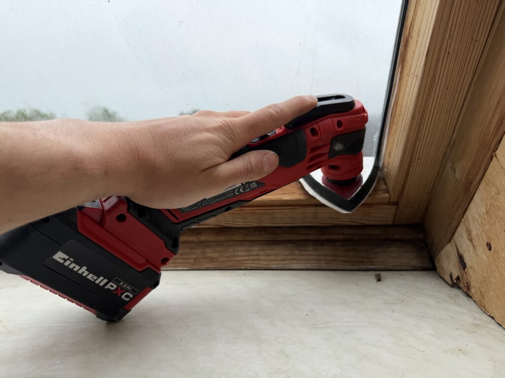 Einhell Varrito Multitool schleift mit Dreieck-Schleifplatte die Ecke eines Holzfensterrahmens