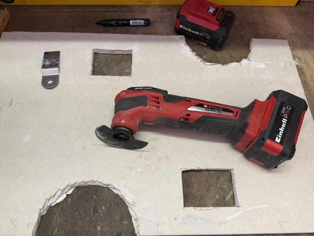 Runde und eckige Ausschnitte in einer Gipskartonplatte mit Einhell Varrito Multitool daneben