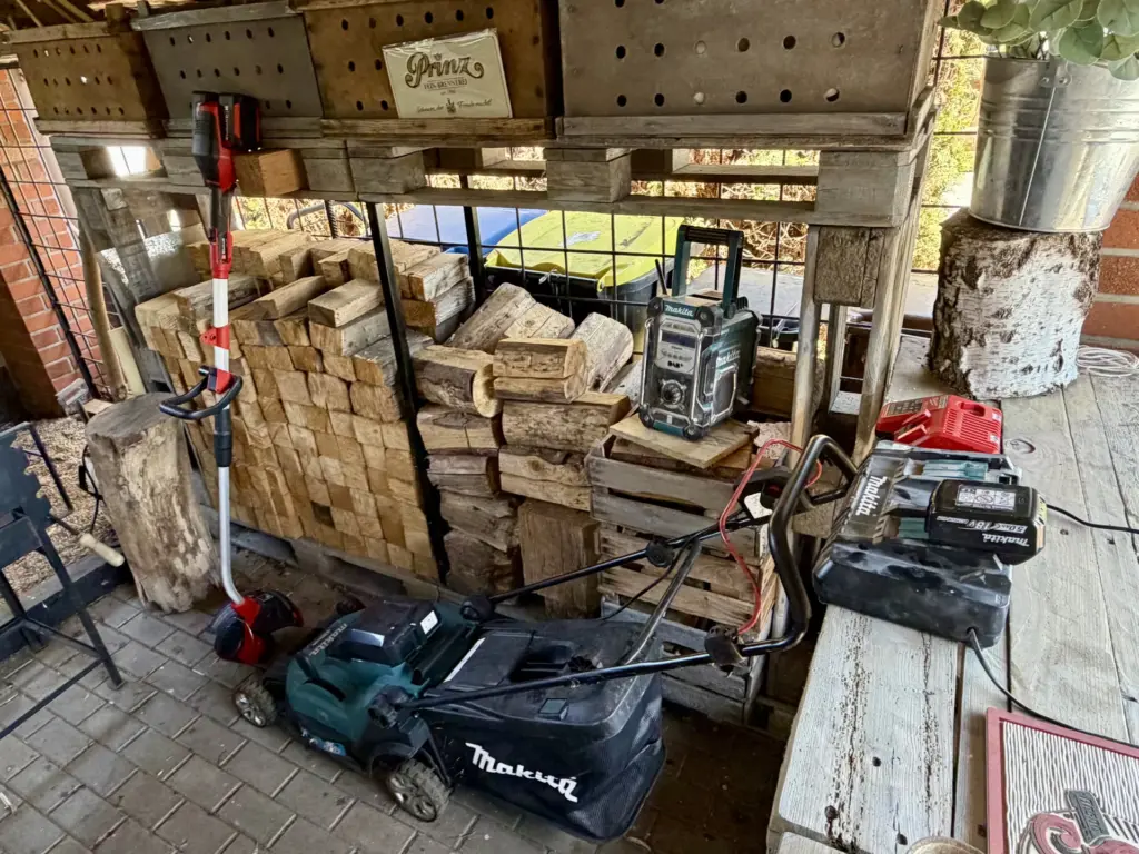 Makita-Mäher und Einhell-Trimmer im Unterstand mit Ladegerät und Wechselakkus für die Gartenarbeit