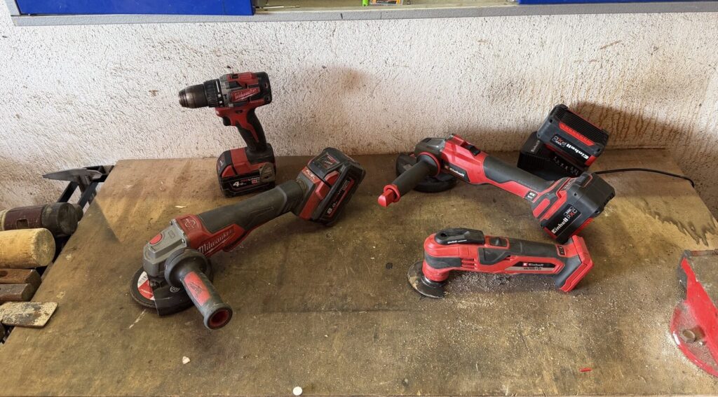 Gebrauchte Milwaukee M18 und Einhell Power X-Change Akkugeräte mit Akkus auf einer Werkbank
