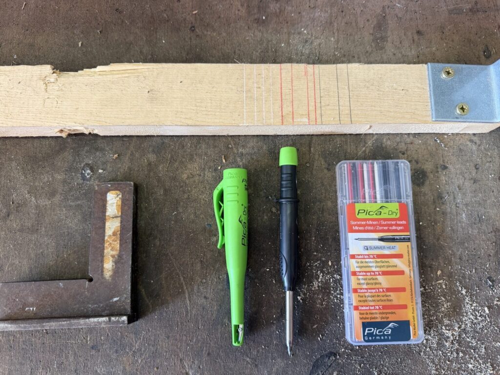 Pica Dry Markierstift mit Ersatzminen neben weißen, roten und schwarzen Markierungen auf einem Holzbrett