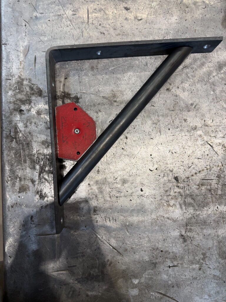 Regalwinkel aus Flachstahl mit Diagonalrohr, fixiert mit rotem Schweißmagnet auf dem Schweißtisch