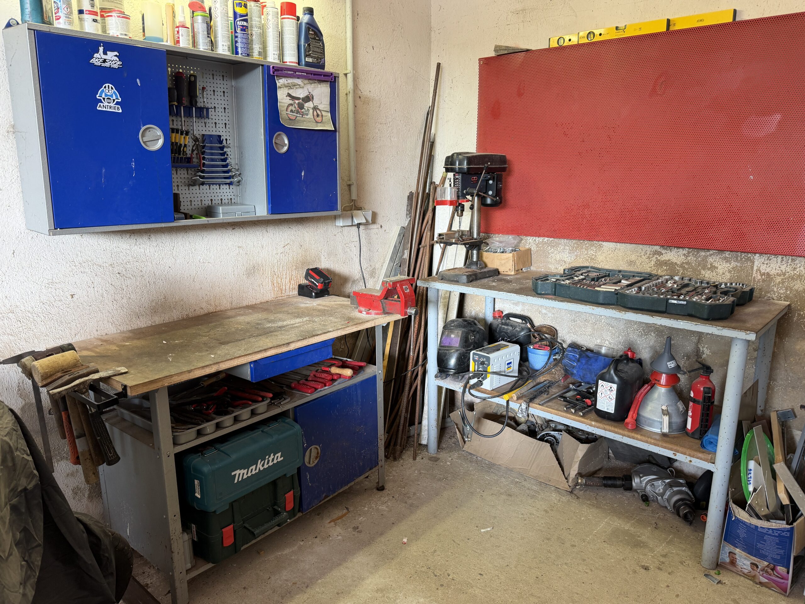 Echte Werkstattecke in einer Garage mit Werkbank, Hängeschränken, Ständerbohrmaschine und großer Lochwand