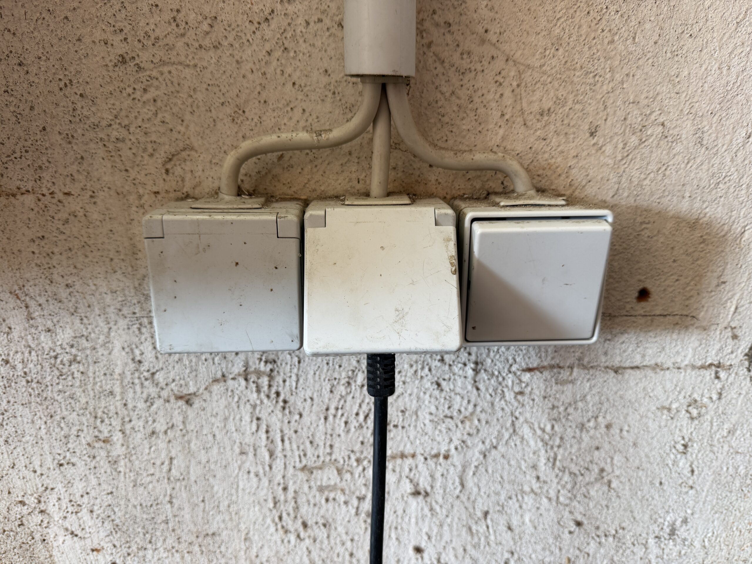 Zwei Aufputz-Steckdosen und ein Lichtschalter an der Wand einer Garagenwerkstatt