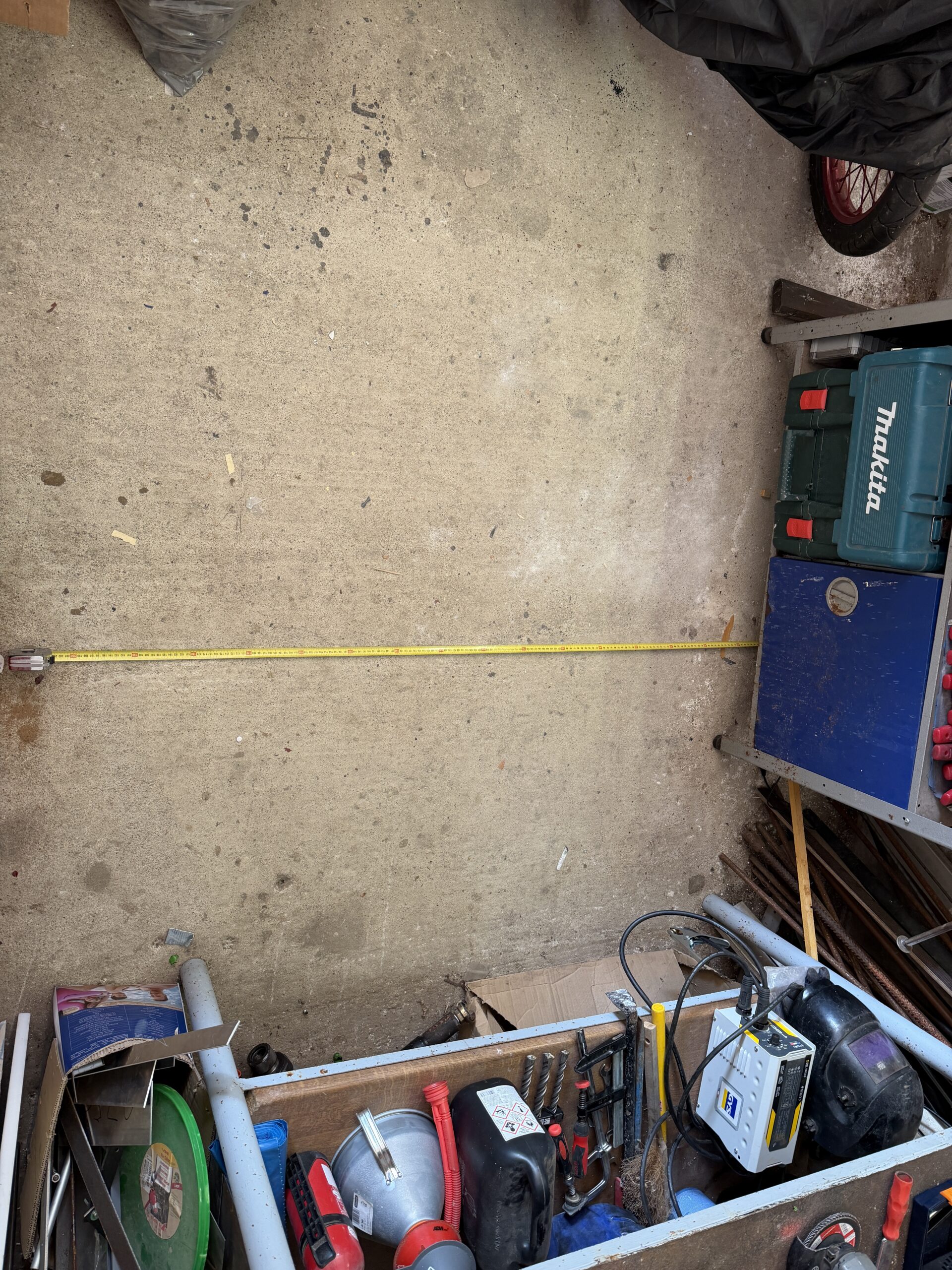 Mit einem Maßband vermessene Fläche einer etwa zwei mal zwei Meter großen Werkstattecke