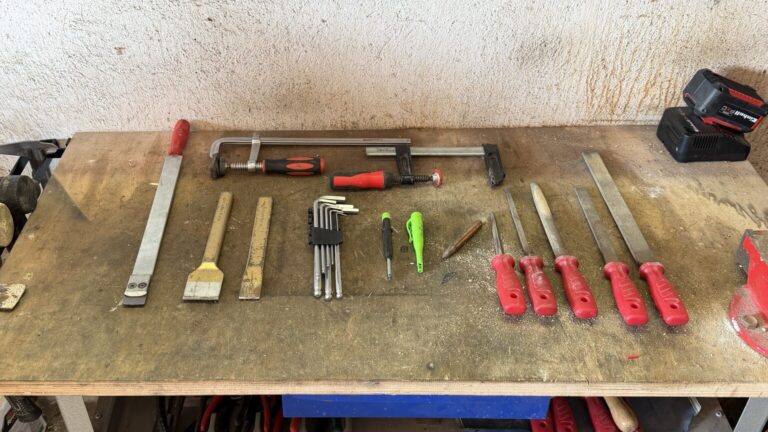Werkzeug-Grundausstattung mit Schraubzwingen, Inbusschlüsseln, Meißeln, Feilen und Markierstiften auf einer gebrauchten Werkbank
