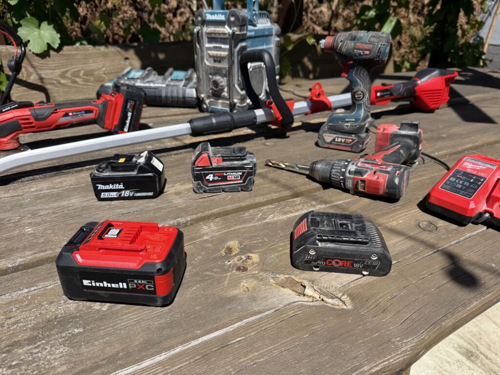 Akkus von Einhell PXC 5,2 Ah, Makita LXT 5,0 Ah, Milwaukee M18 4,0 Ah und Bosch ProCORE 4,0 Ah auf einem Holztisch.
