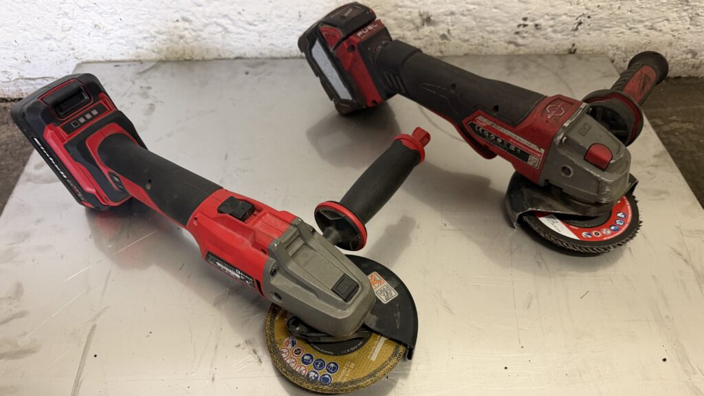 Einhell AXXIO 18/125 vorne links und Profi-Winkelschleifer hinten rechts mit Akkus und Zusatzhandgriffen auf der Werkbank.