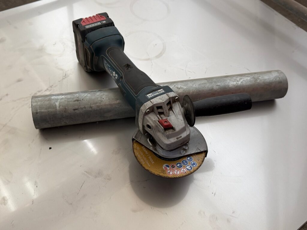 Bosch Professional Akku-Winkelschleifer GWS 18V-7 mit Gebrauchsspuren, 18-V-Akku und gelber Trennscheibe für Stahl und Inox, quer über einem Rohr auf einem Blech