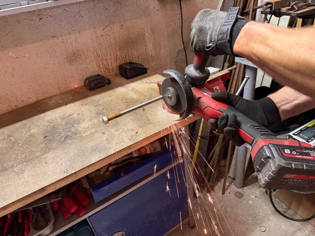 Milwaukee M18 Akku-Winkelschleifer mit 8-Ah-Akku beim Trennen eines Metallstabs, Funkenflug an der Werkbank
