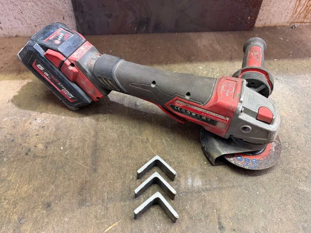 Milwaukee M18 FSAGV125XPDB mit 5,5-Ah-Akku neben drei abgetrennten Stücken Winkelstahl